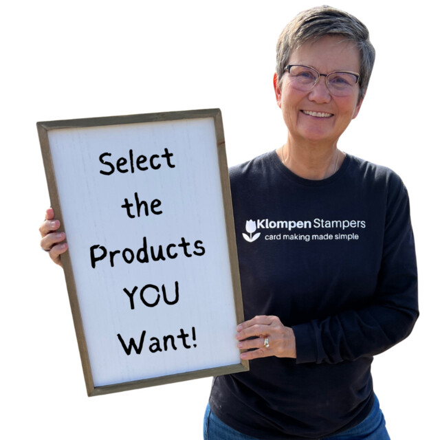 Jackie of Klompen Stampers holding a sign to share Stampin' Up! benefits that reads "select the products you want"